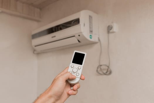 The guy's hand holds the remote control of the air conditioner. Cooling and temperature control in the room of the house.