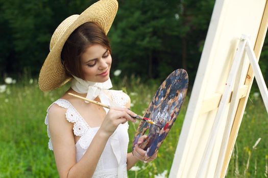 pretty woman in hat artist paints a picture on nature paint. High quality photo