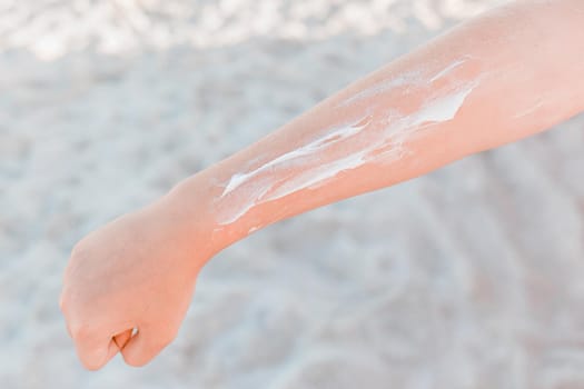 The hand of a young girl with a white pattern of sunscreen and protection from sunlight against the background of beach sand.