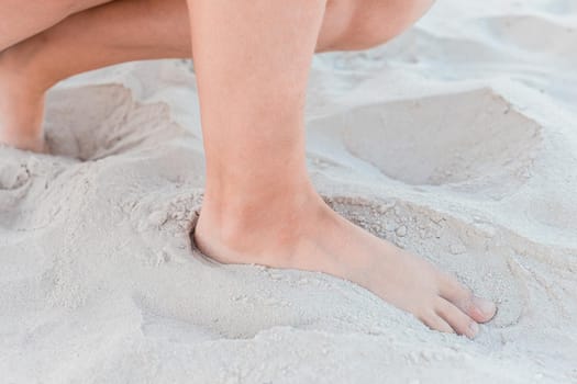 A young girl sat down her legs standing on the warm white beach sand background close-up.