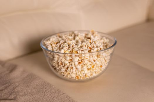 Bowl of popcorn for watching a film on a beige couch. Snacks and unhealthy junk food.