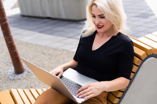 Young woman wearing smartwatch using laptop computer. Female working on laptop in an outdoor cafe