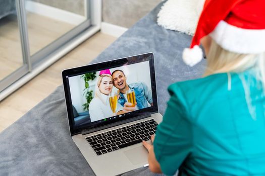 Smiling girl wearing Santa hat having video calling family by webcam. Woman with laptop sitting on kitchen at home using virtual meeting chat on holidays. Happy Christmas and New Year new normal