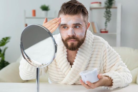 Closeup of handsome young man applying facial cream in front of mirror