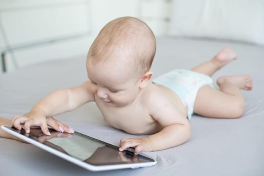 A six-month baby with a tablet computer, looking at screen, at home.