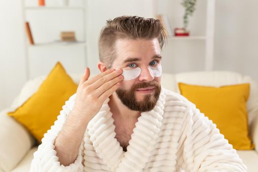 Bearded man applying eye patches on his face. Wrinkles and face home care for men