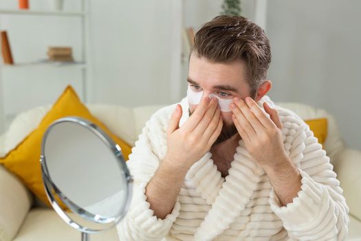 Bearded man applying eye patches on his face. Wrinkles and face home care for men