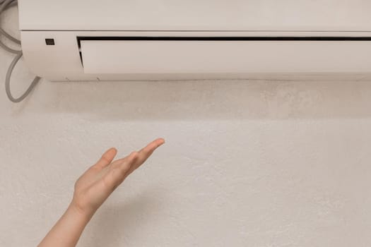 The girl puts his hand under the air conditioner in the room to check the temperature and the feeling of warm or cold air.