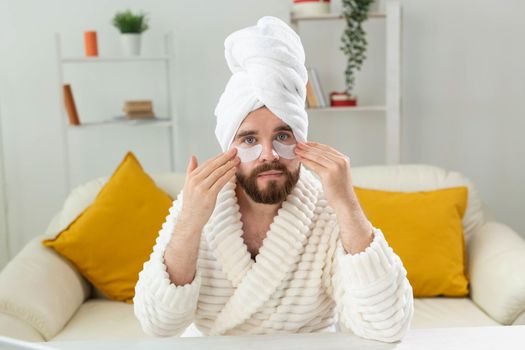 Bearded man applying eye patches on his face. Wrinkles and face home care for men