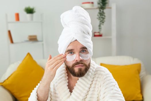 Young man with patches under the eyes at home. Concept of cosmetology for men.Spa at home, body and skin care.