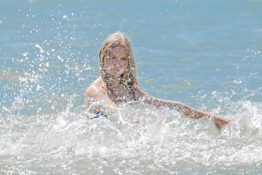 Young cheerful girl teenager blonde European appearance makes splashes of water with her hands in the sea.