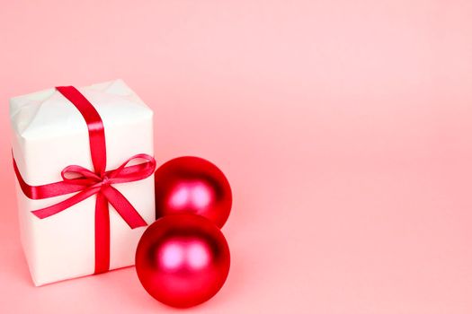 Gift wrapped with white paper and pink bow next to Christmas decoration on pink background