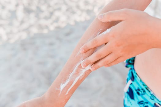 The hand of a young girl smears sunscreen and sun protection on the second hand against the background of the beach, close-up.