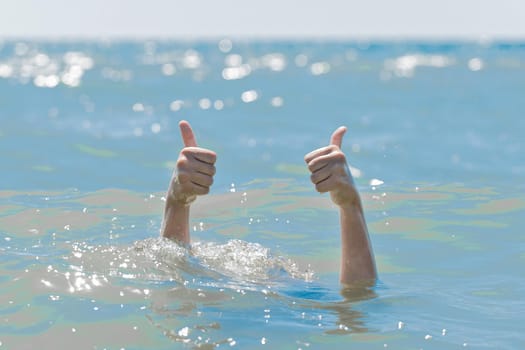 Hands from under the water of a drowning girl shows class with a thumb up. Help and urgent rescue of a person during a dangerous swimming, sos.