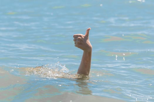 Hand from under the water of a drowning girl shows class with a thumb up. Help and urgent rescue of a person during a dangerous swimming, sos.