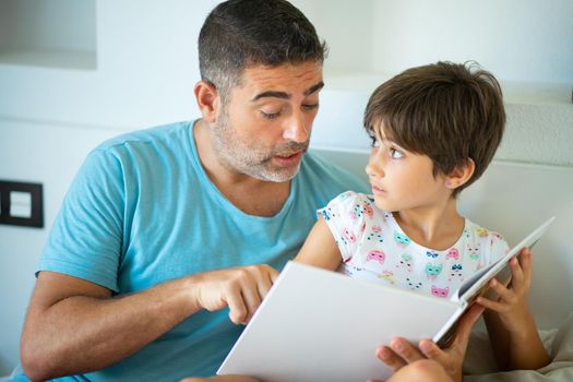 Funny dad and lovely little girl are having fun on the bed. Middle-age father with her eight years daughter using digital tablet in bedroom.