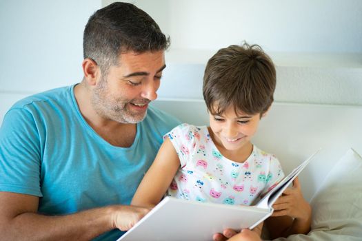 Middle-age father with her eight years daughter using digital tablet in bedroom. Funny dad and lovely little girl are having fun on the bed.
