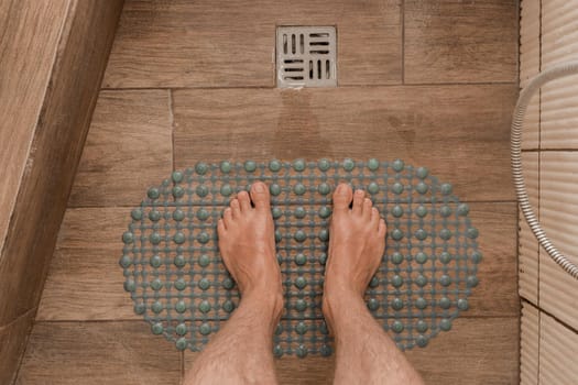 Men's feet stand on a plastic anti-slip mat next to the floor drain in the bathroom or shower.
