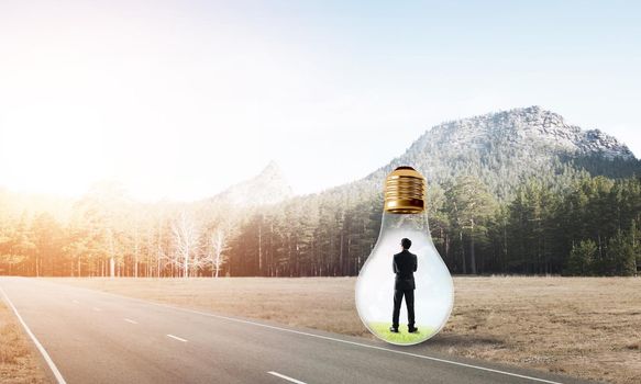 Young businessman trapped inside of light bulb on asphalt road
