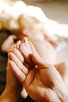 Close up of newborn babe barefoot feet with mother arm. Concept of maternity, newborn photo session and babies, family. Selective focus