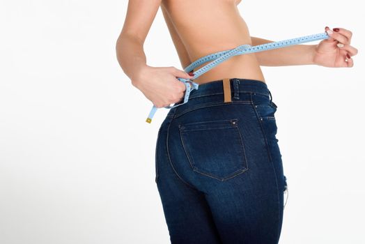 Young woman measuring waist with a tape. Fit and healthy girl with blue jeans on white background.