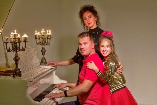 Happy family on Christmas Eve near the old white piano on which candles are burning. New Year concept, family holiday.