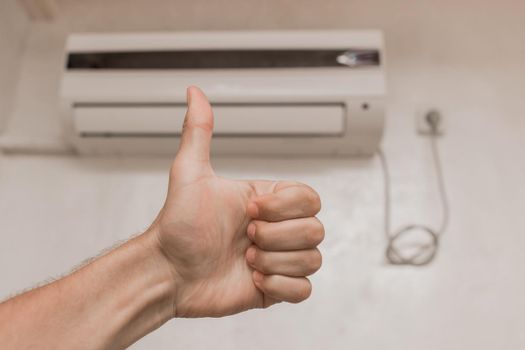 The guy's hand shows the class thumbs up against the background of the air conditioner on the wall in the room background.