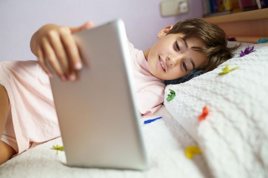 Cute girl, eight years old, using a tablet computer in her bedroom. Girl with short hair.