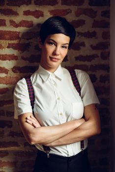 Beautiful young woman, model of fashion, with very short haircut, looking at camera with a brick wall in the background. Beauty and hairstyles concept.