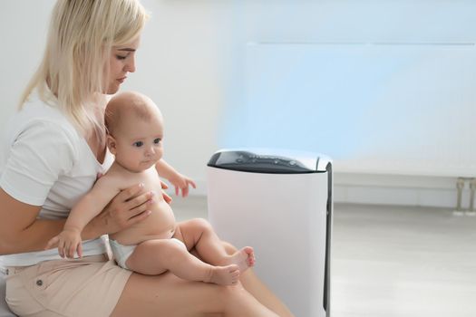 mother and baby near air purifier at home.