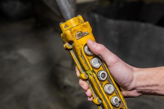 The hand of a working man holds the control panel of the crane lifting mechanism at an industrial plant.