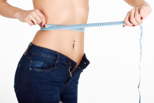 Young woman measuring waist with a tape. Fit and healthy girl with blue jeans on white background.