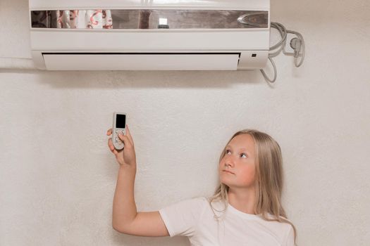 Young girl cute blonde teenager of European appearance holds in his hands a remote control of air conditioning in the interior of the room.