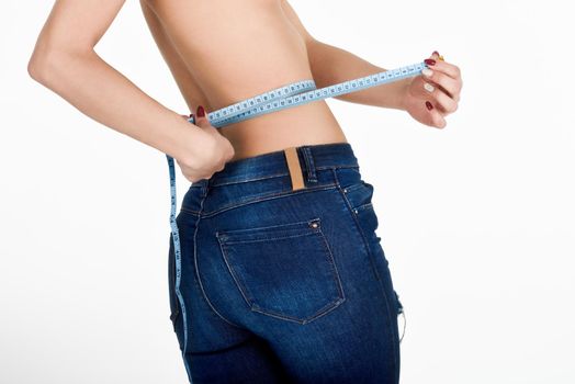 Young woman measuring waist with a tape. Fit and healthy girl with blue jeans on white background.