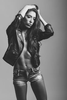 Beautiful woman body in denim jeans shorts and black leather jacket. Black and white studio shot.