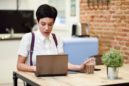 Young woman with very short haircut typing with a laptop at home. Businesswoman working at home concept.