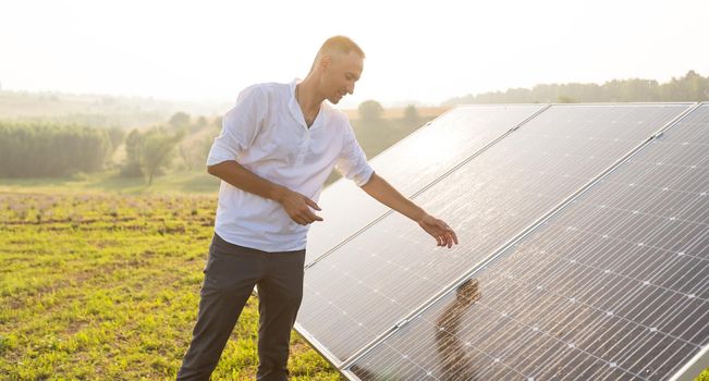 oung engineer is checking an operation of sun and cleanliness of photovoltaic solar panels on a sunset. Concept: renewable energy, technology, electricity, service, green, future.