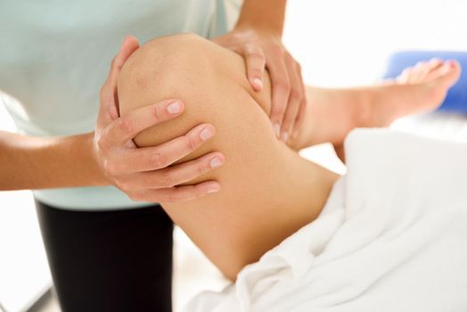 Medical massage at the leg in a physiotherapy center. Female physiotherapist inspecting her patient. Close-up photograph.