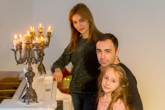 Happy Family Posing in Luxurious Interior near Piano Decorated with Burning Candles in Candlestick, Portrait of Parents and Charming Girl, Father Gently Looking at His Adorable Daughter