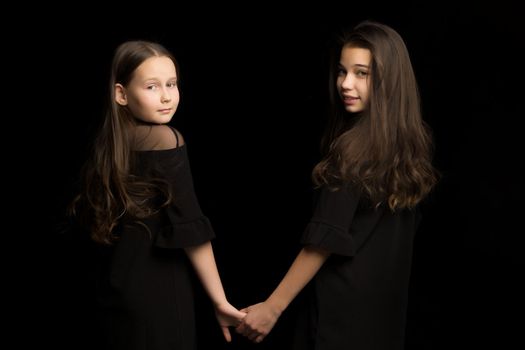 Two cute little girls are holding hands. Studio photography on a black background.