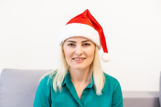 A young smiling woman wearing red Santa Claus hat making video call on social network with family and friends on Christmas day.