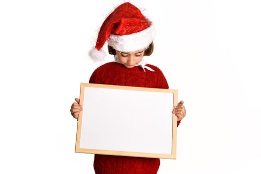 Little girl wearing santa hat holding blank board for advertisementon on white background. Invitation to christmas activities. Winter clothes