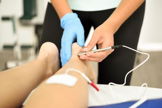 Electroacupuncture dry with needle connecting machine used by acupunturist on female patient for acupuncture guided by EPI Intratissue Percutaneous Electrolisis. Electro stimulation in physical therapy to ankle of a young woman in physiotherapy center.