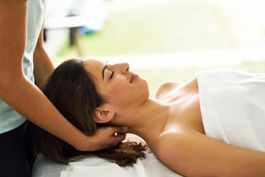Young caucasian smiling woman receiving a head massage in a spa center with eyes closed. Female patient is receiving treatment by professional therapist.