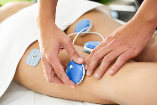 Physiotherapist applying electro stimulation in physical therapy to a young woman. Medical check at the leg in a physiotherapy center.