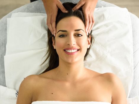 Top view of young caucasian smiling woman receiving a head massage in a spa center. Female patient is receiving treatment by professional therapist.