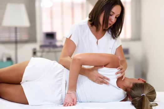 Professional female physiotherapist giving shoulder massage to blonde woman in hospital. Medical check at the shoulder in a physiotherapy center.