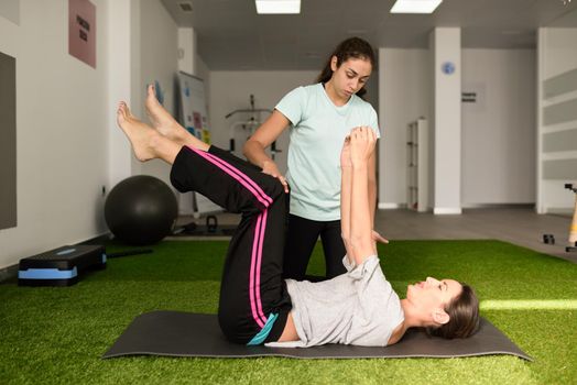 Physical therapist assisting young caucasian woman with exercise during rehabilitation in the gym at hospital. Female physiotherapist training a patient in physiotherapy center.