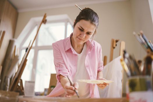 Female artist working in studio. Creative workspace, painting class, easel with canvas, art therapy. Inspiration, creativity, talent, craft concept. Artist studio interior. People, leisure and hobby.