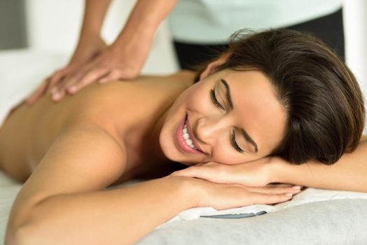 Young female receiving a relaxing back massage in a spa center. Brunette woman patient is receiving treatment by professional therapist.